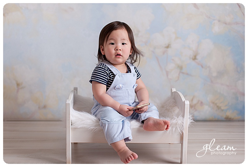 Baby in studio sitting on a little doll bed