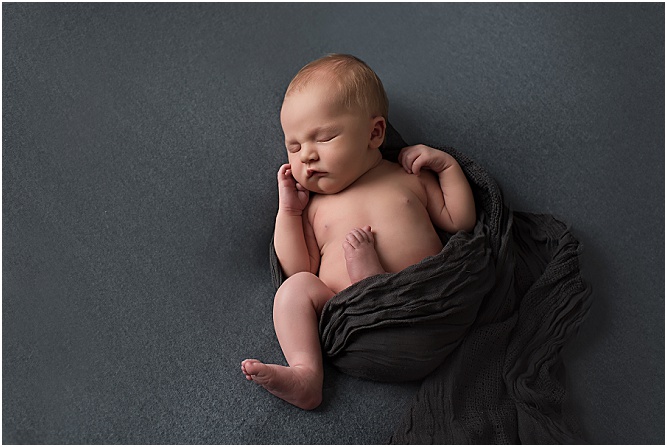 Newborn baby wrapped in a wrap sleeping on a grey blanket