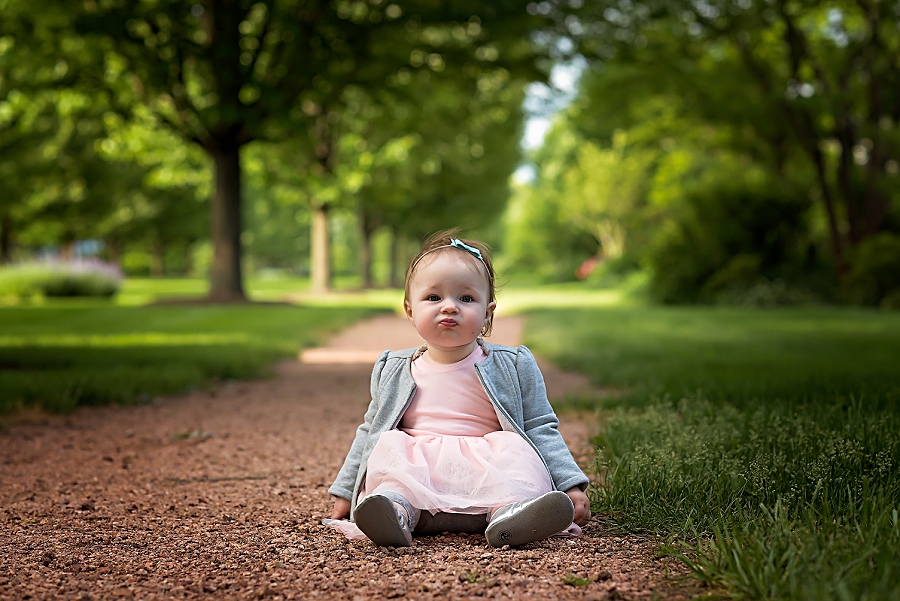 Cute baby girl sitting on a stone path with grass all around