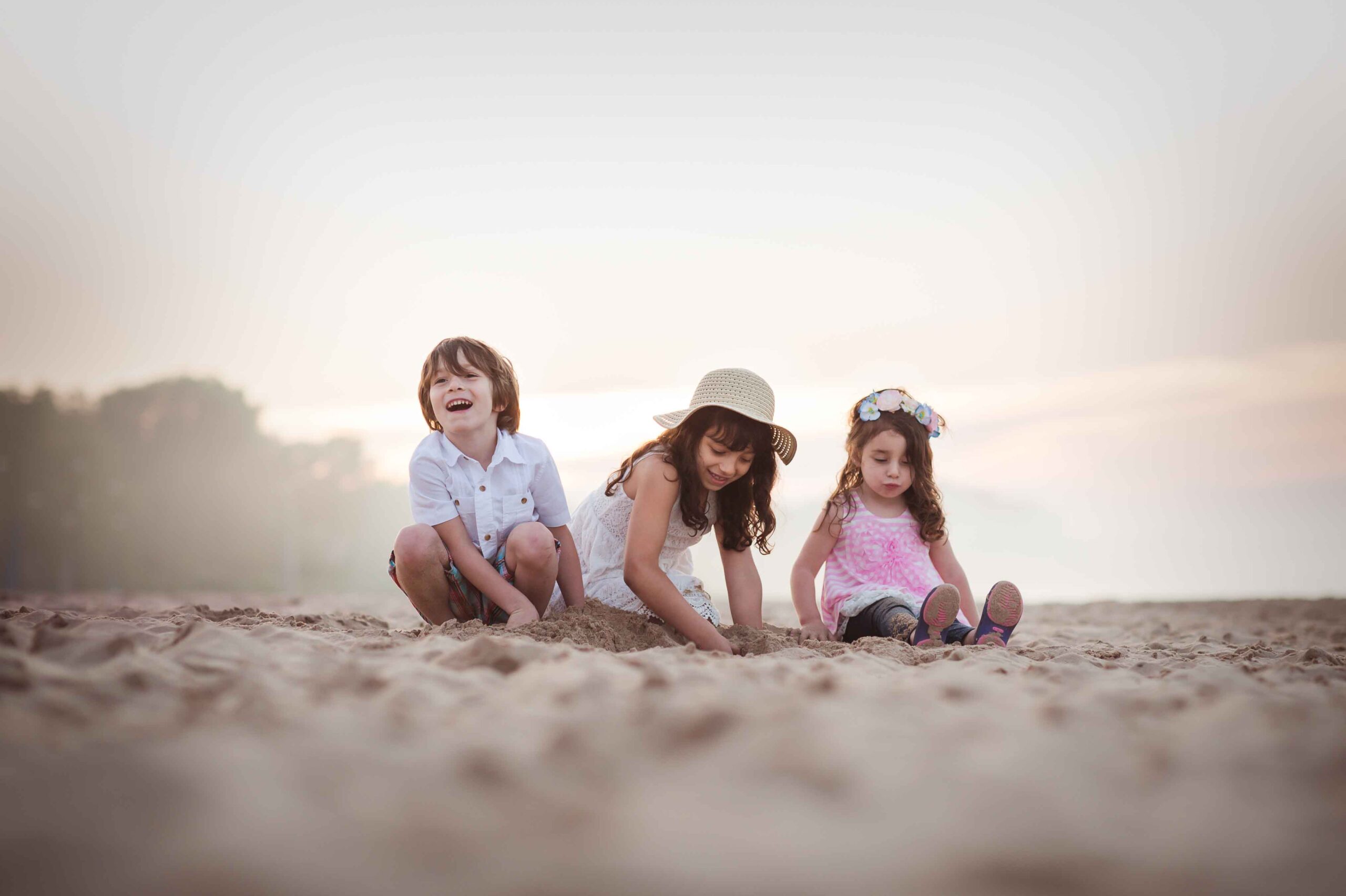 Three siblings digging in sand on a beach